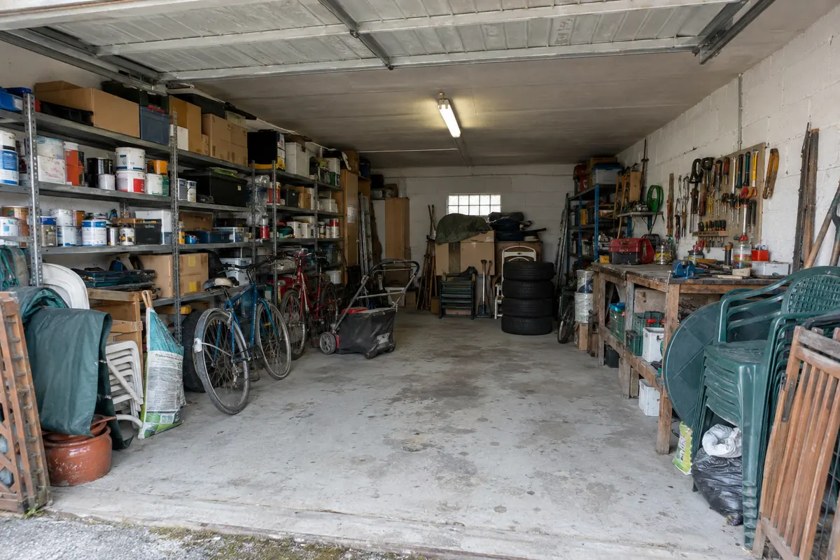 Garage de pavillon encombré d'étagères, de pots de peinture, de vélos, de pneus et d'outils avant le débarras