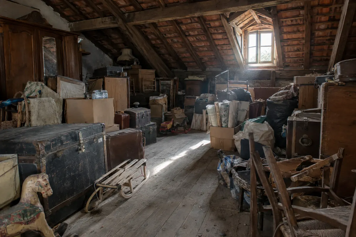 Grenier sous charpente encombré de malles, de cartons, de meubles et de jouets anciens avant le débarras