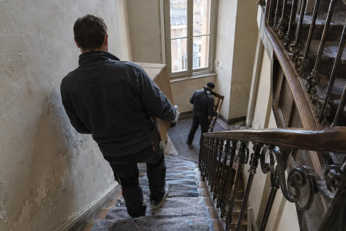Intervenants descendant cartons et chaises dans la cage d'escalier en bois d'un immeuble ancien d'Albi